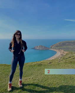 A slim build lady with long brown hair smiles at the camera on the Jurassic Coast coastal path